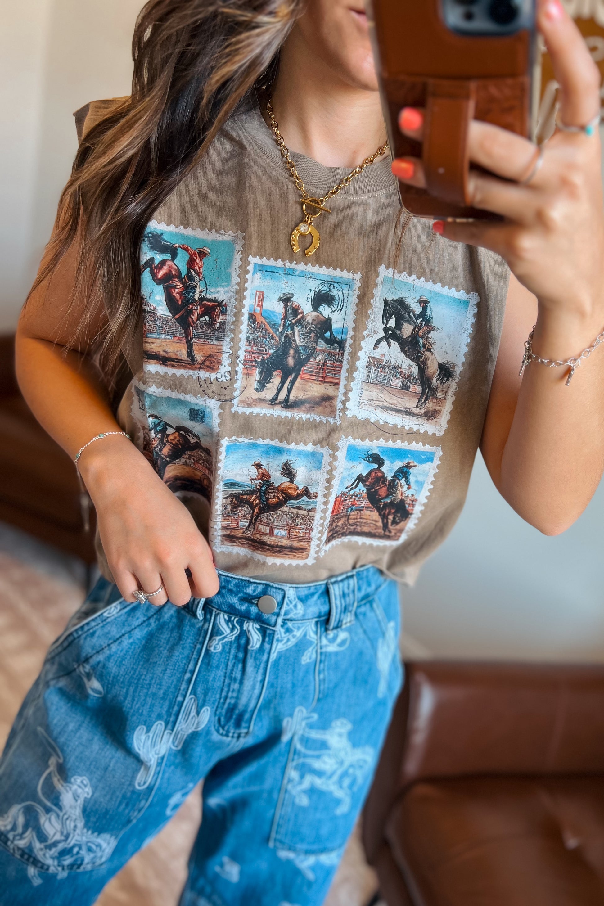 Brown sleeveless muscle tank featuring a vintage rodeo stamp graphic with six cowboy and bronc riding scenes, styled with blue western-print jeans.