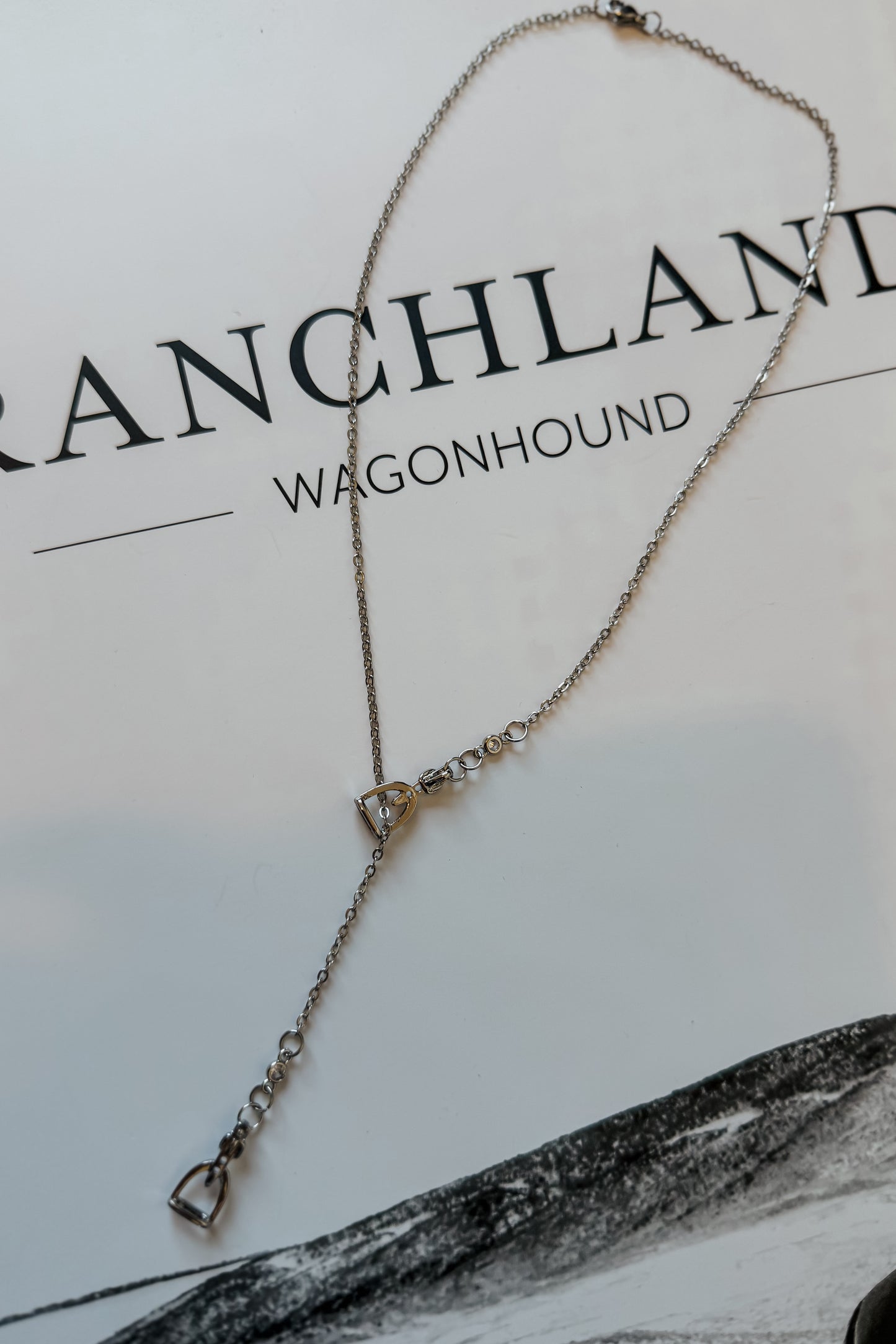 Close-up of silver stirrup lariat necklace showing dainty chain and slider detail.