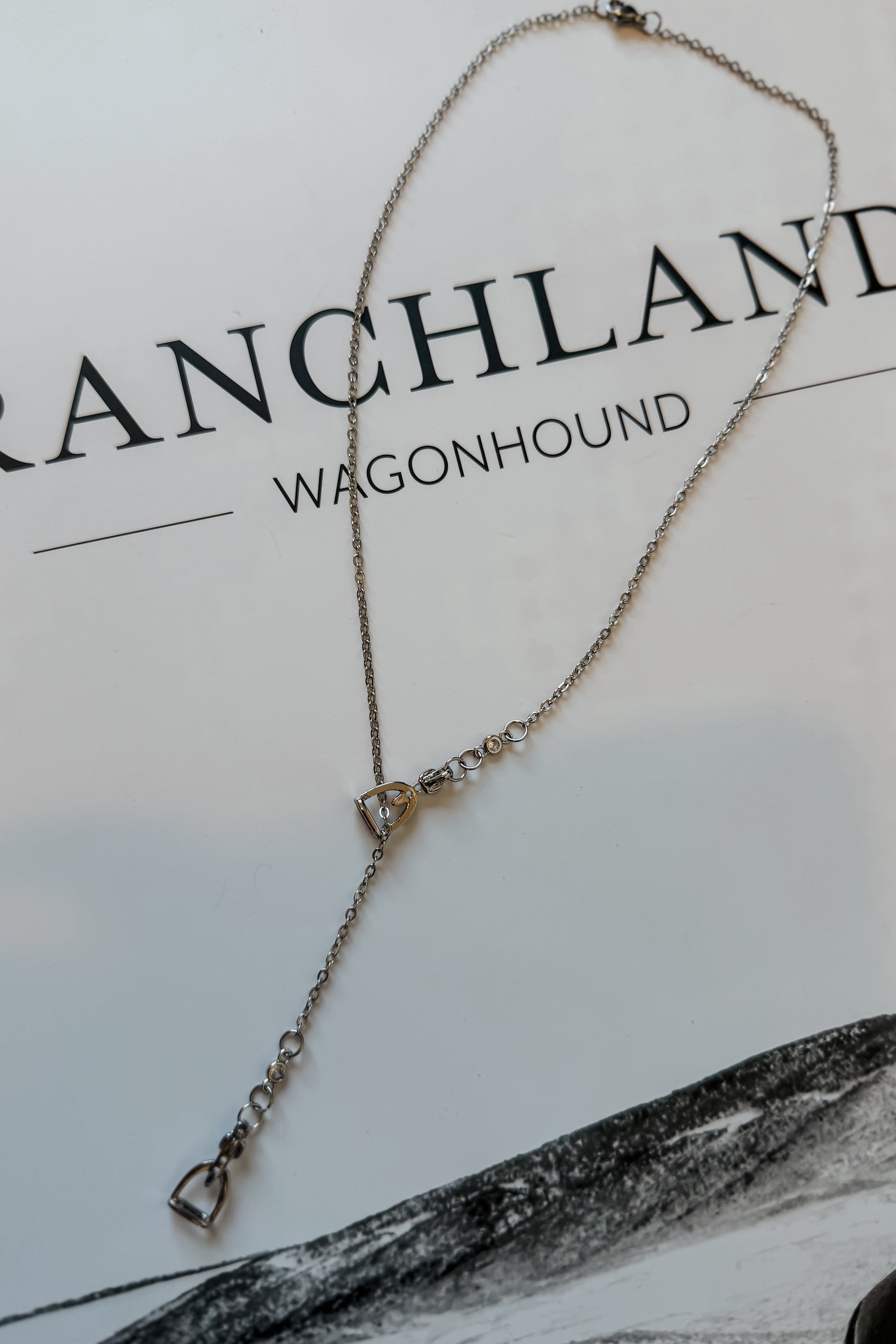 Close-up of silver stirrup lariat necklace showing dainty chain and slider detail.