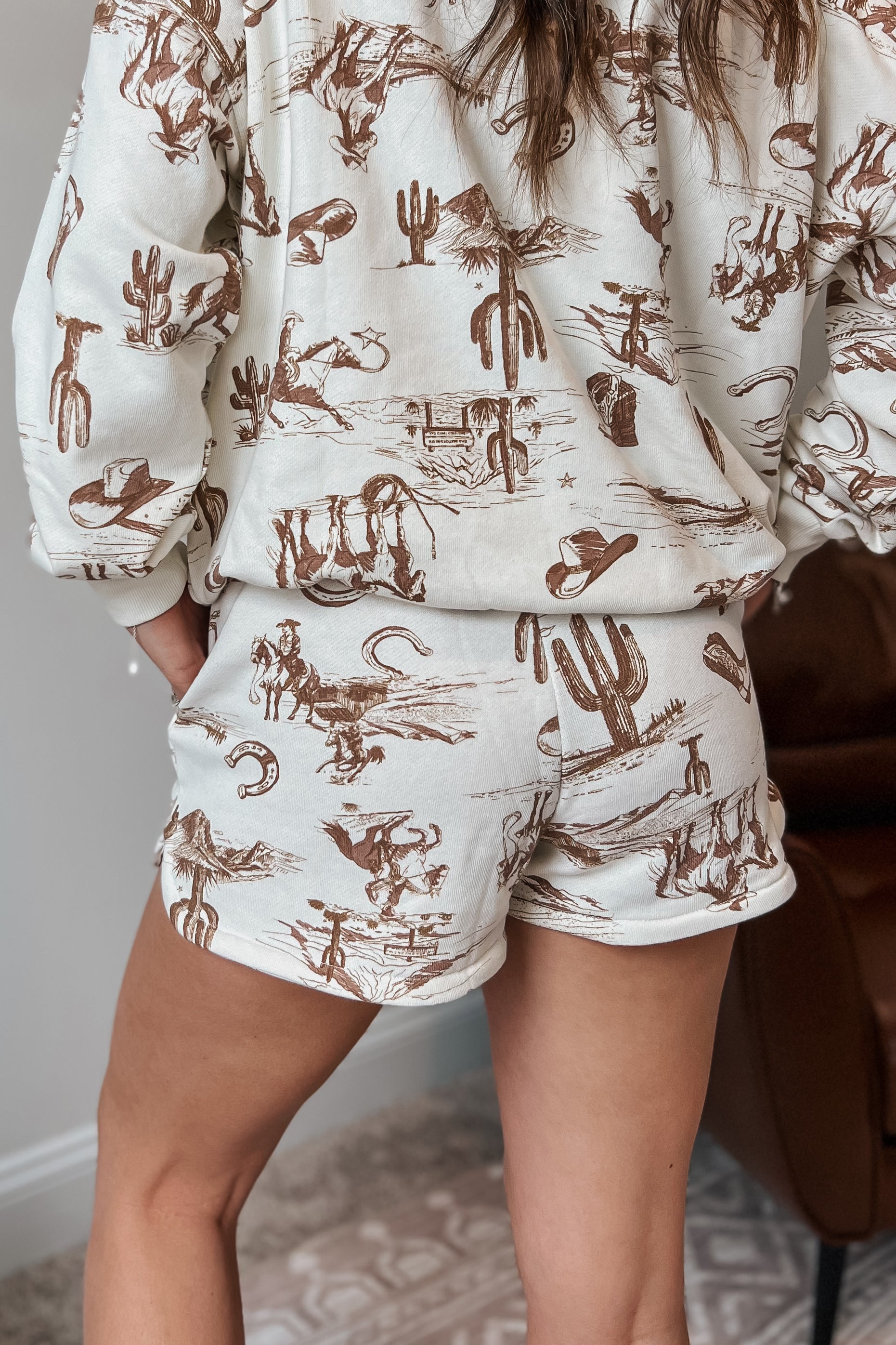 Cream elastic-waist shorts with brown western sketch print and side pockets.
