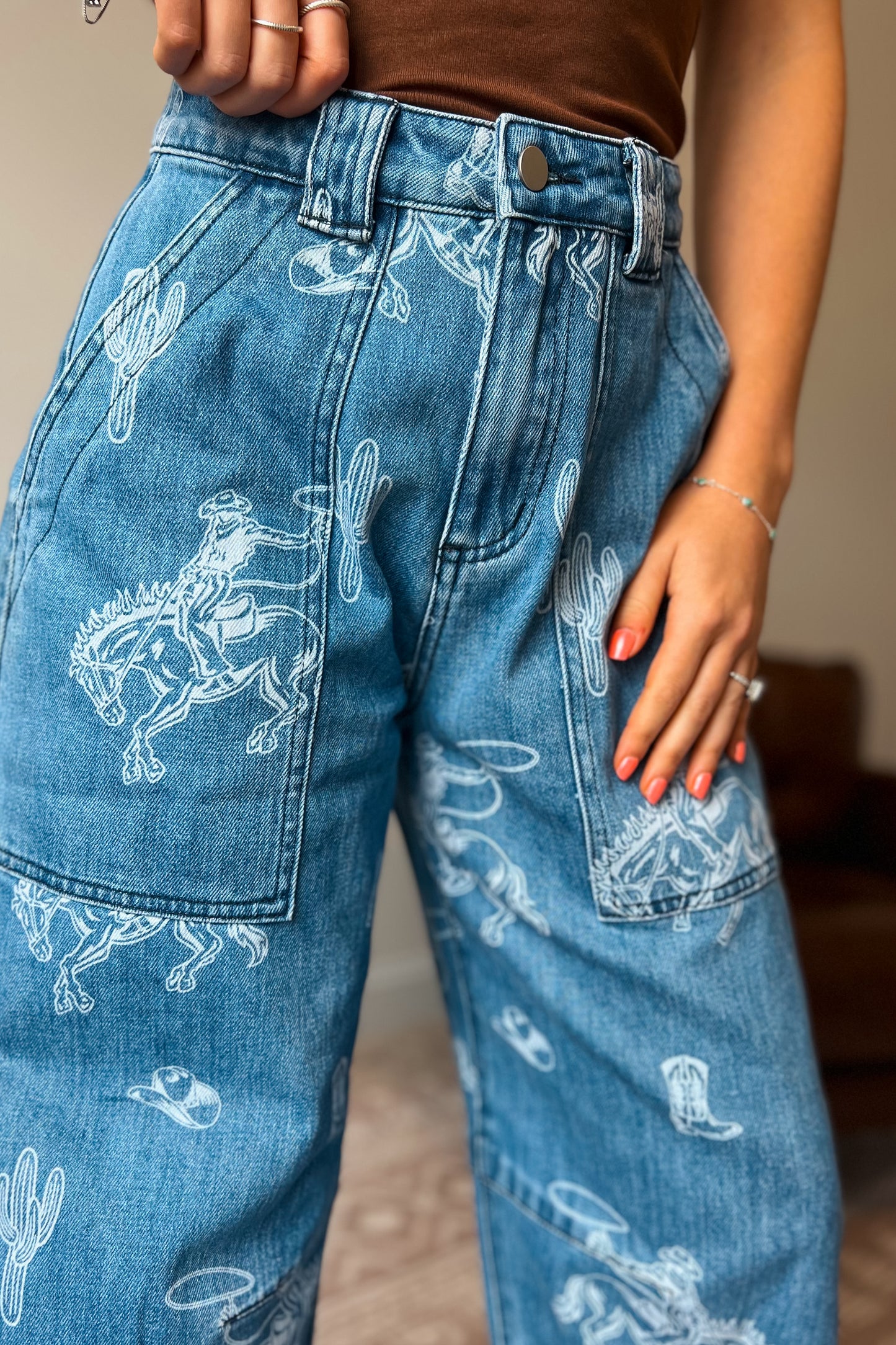 Close-up of western-inspired denim jeans featuring cowboy, cactus, and rodeo print