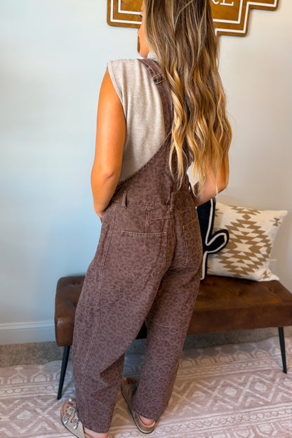 A woman shown from the back wearing brown overall-style pants with a subtle tonal pattern, paired with a light beige sleeveless top.