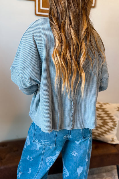 A person shown from the back wearing a light blue ribbed knit sweater and blue jeans