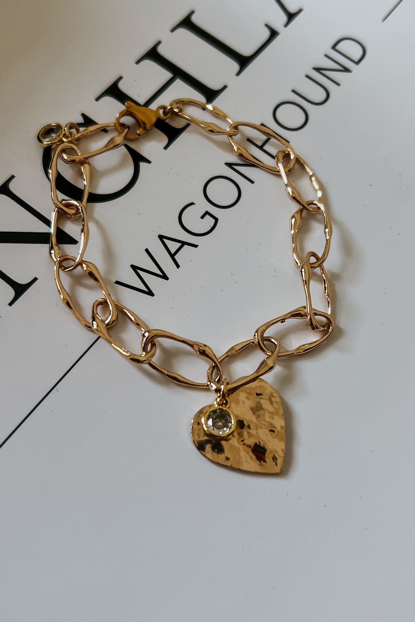Gold chain bracelet featuring hammered heart charm with crystal detail

