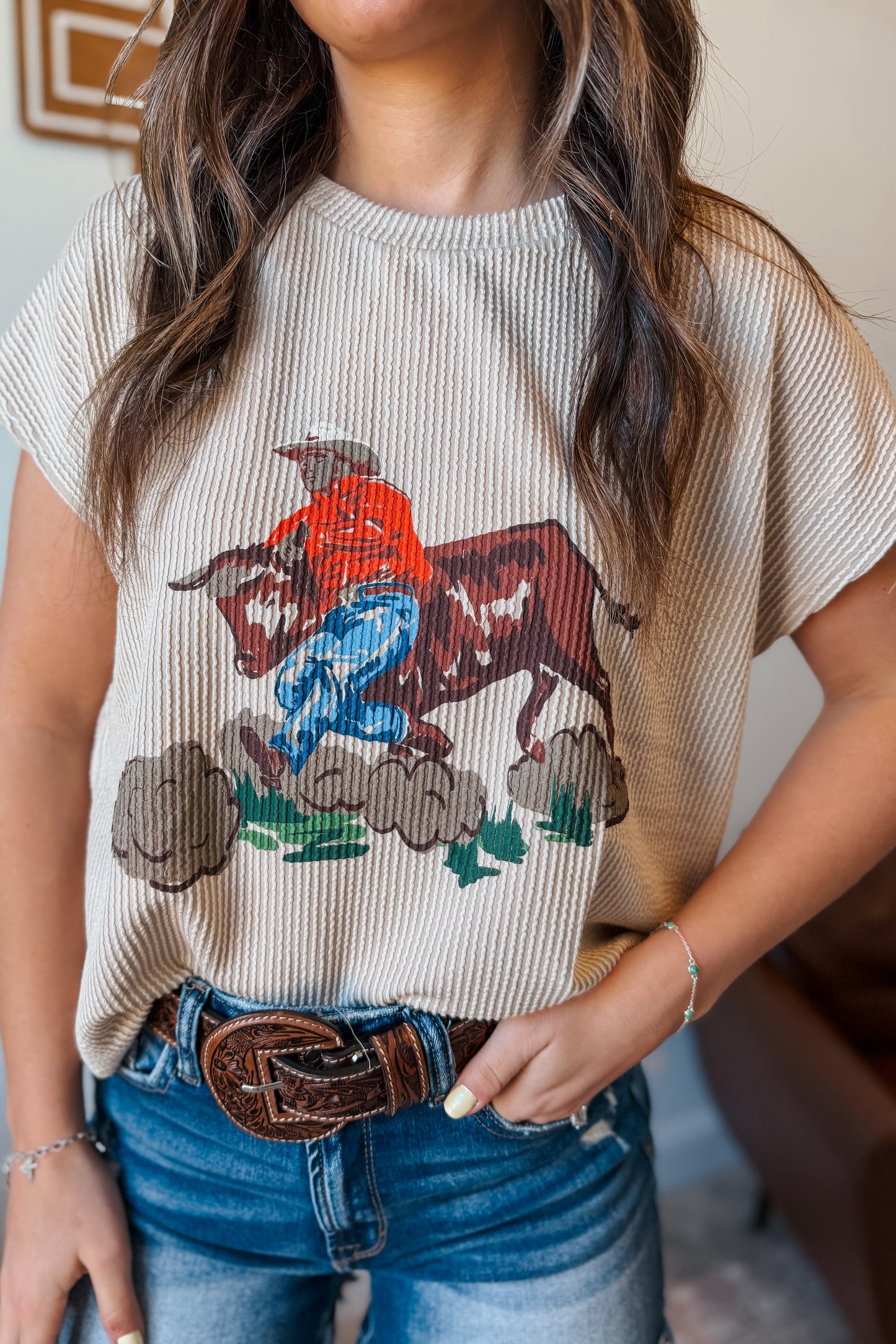 Close-up of cream ribbed fabric top featuring a western graphic of a cowboy steer wrestler