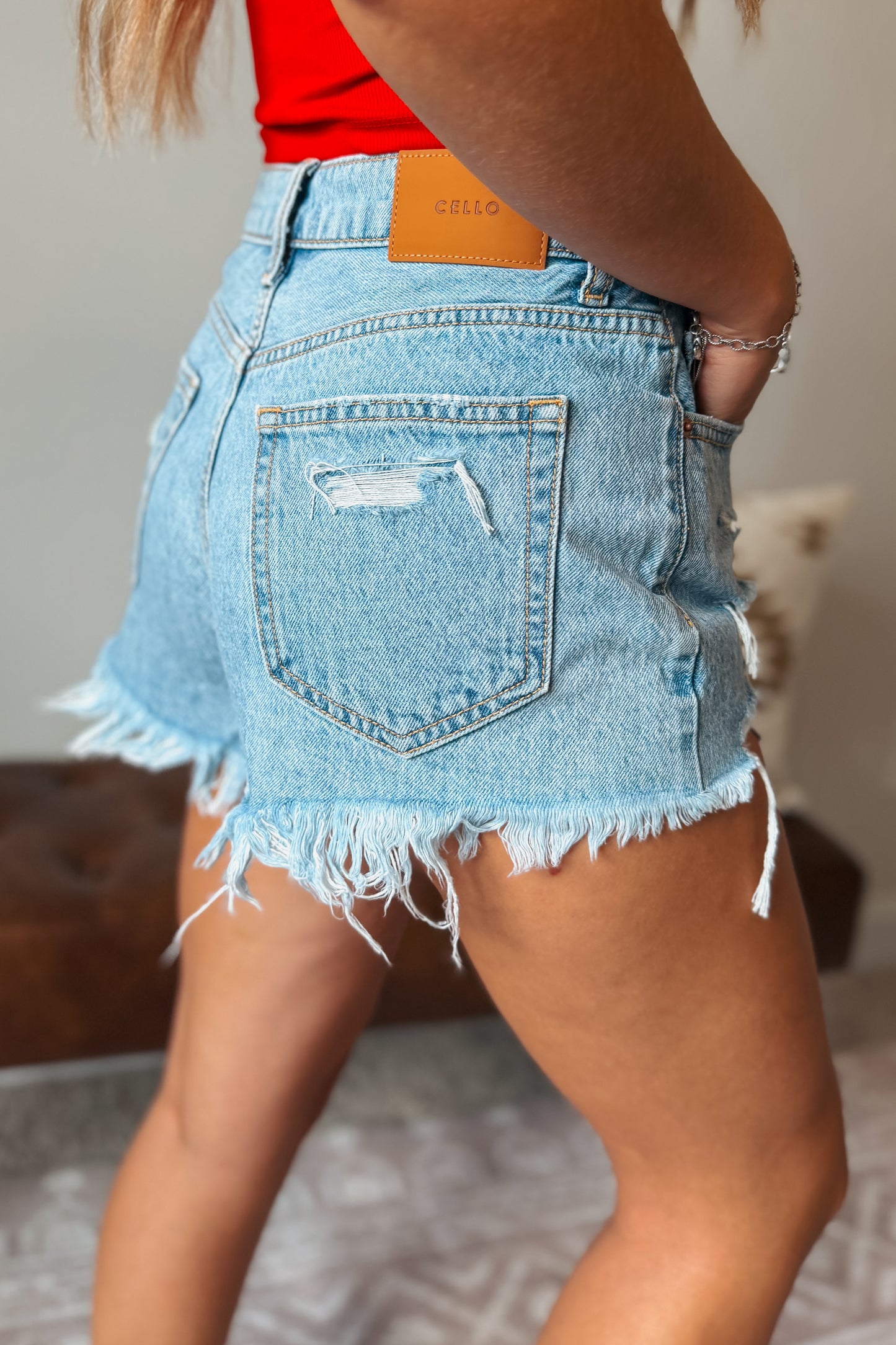 Side view of Cello high-rise light wash distressed denim shorts with a 10.75-inch rise, frayed cutoff hem, and flattering fitted silhouette.
