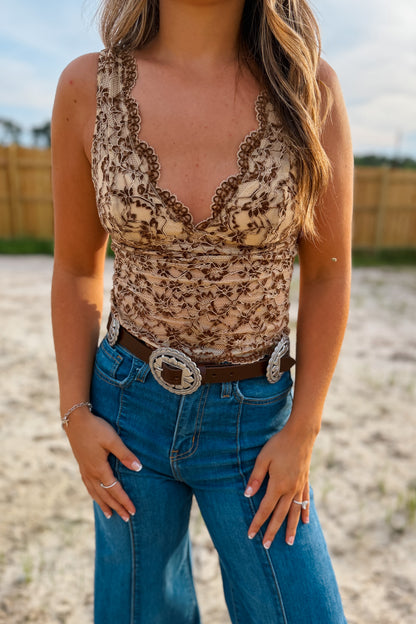Woman wearing a brown and tan floral tank top and blue jeans with a belt
