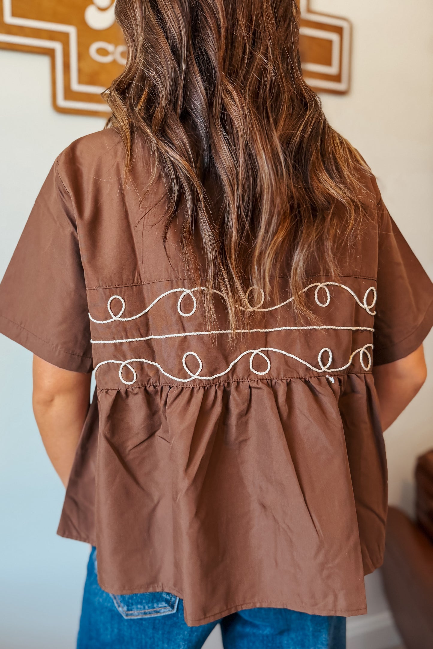 Back view of brown pearl snap button-up babydoll top with short sleeves.