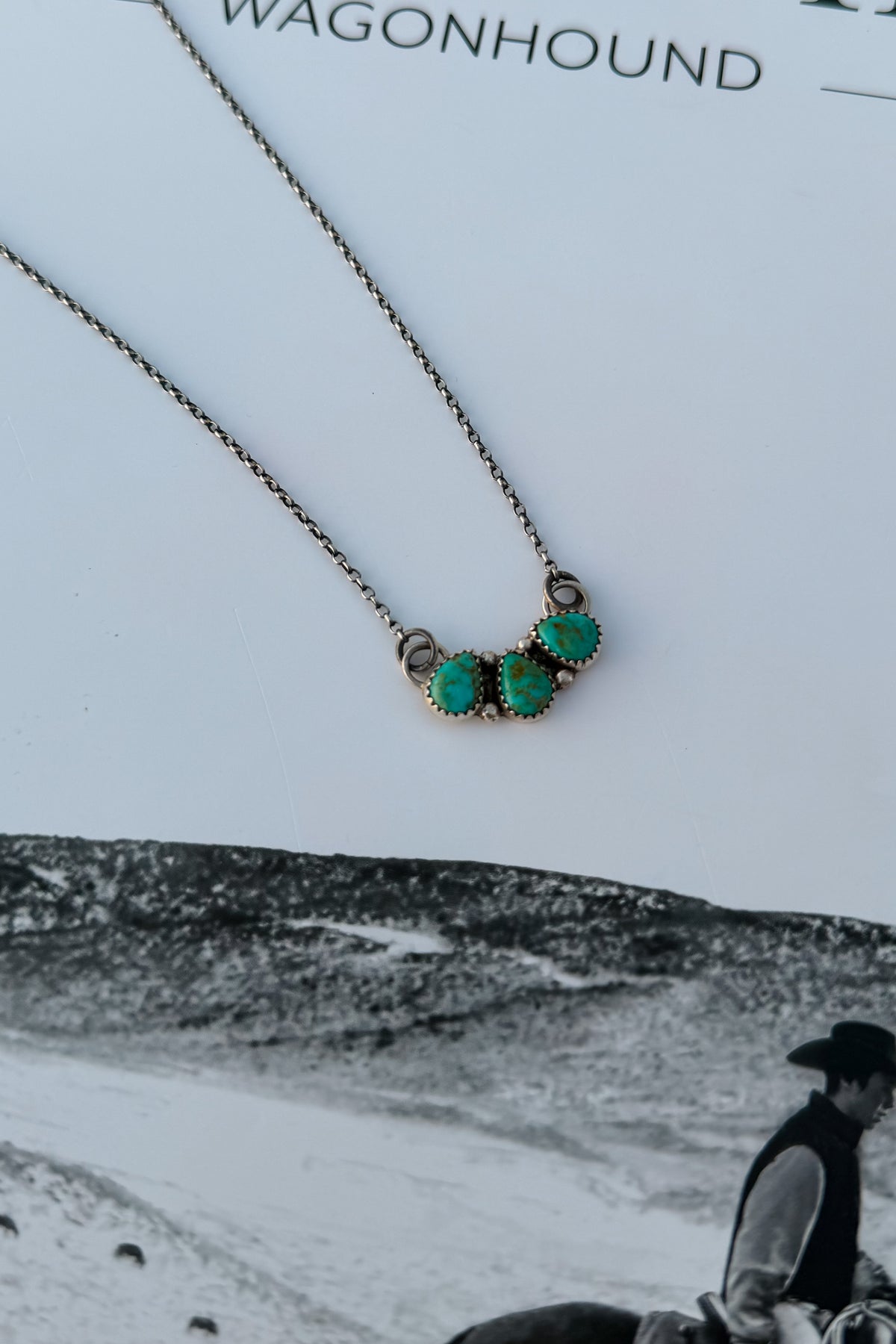 A close-up of a necklace with three oval turquoise-like stones set in a silver-toned metal