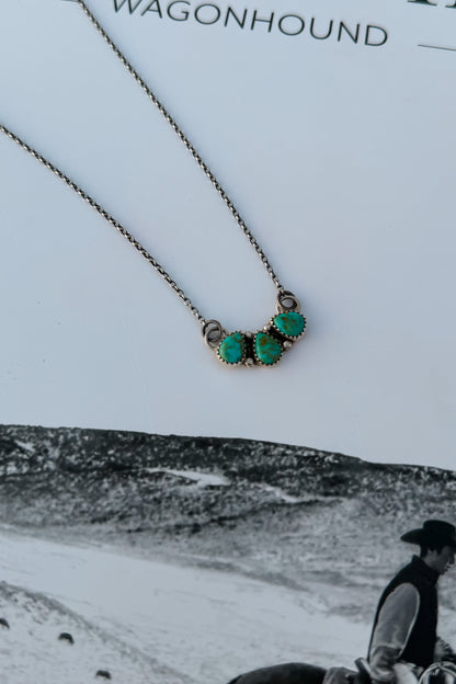 A close-up of a necklace with three oval turquoise-like stones set in a silver-toned metal
