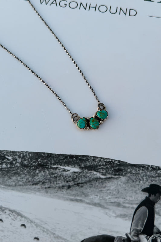 A close-up of a necklace with three oval turquoise-like stones set in a silver-toned metal