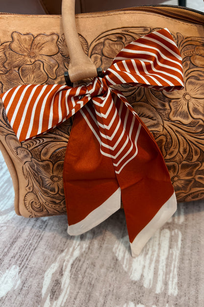 Rust and cream striped Twilly tied in a bow on tooled leather purse strap