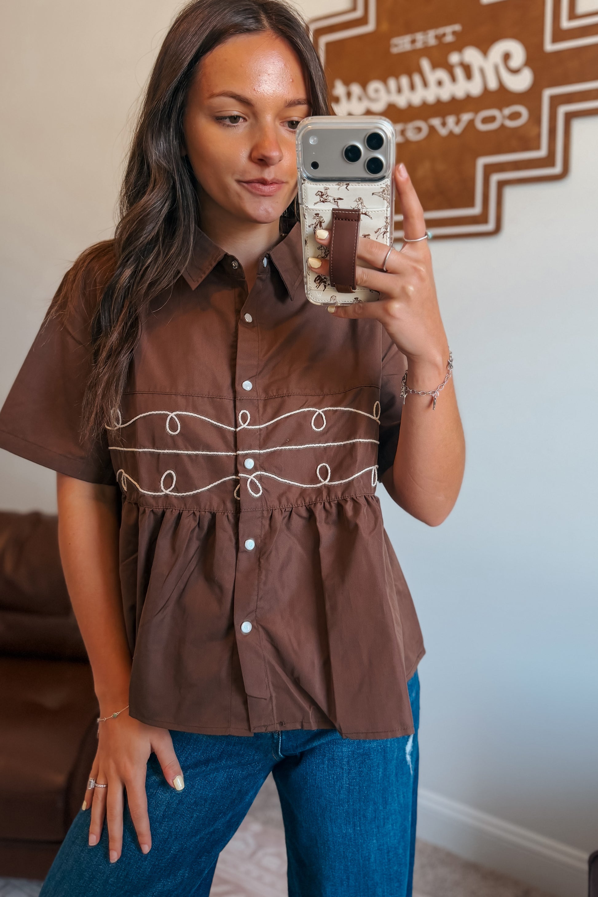 Front view of brown pearl snap short-sleeve babydoll top with embroidered rope detail through the middle.