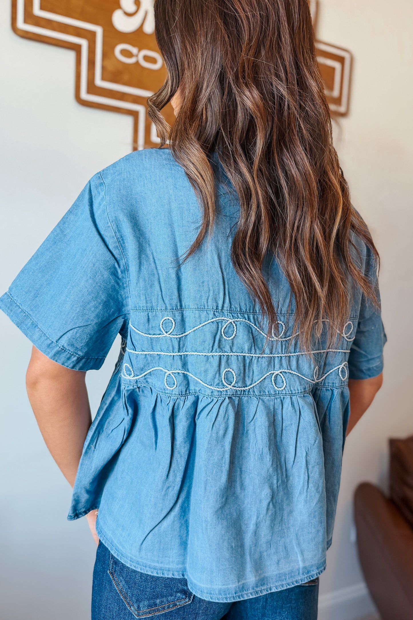 Back view of a light wash denim babydoll-style short sleeve top, plain design with relaxed fit, casual Western-inspired outfit