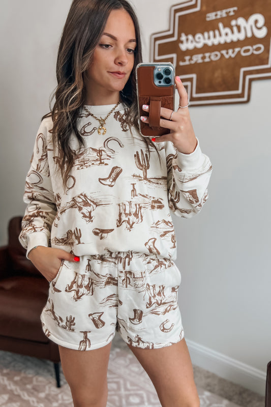 Cream long-sleeve sweatshirt with brown western sketch print, paired with matching elastic-waist shorts with side pockets.