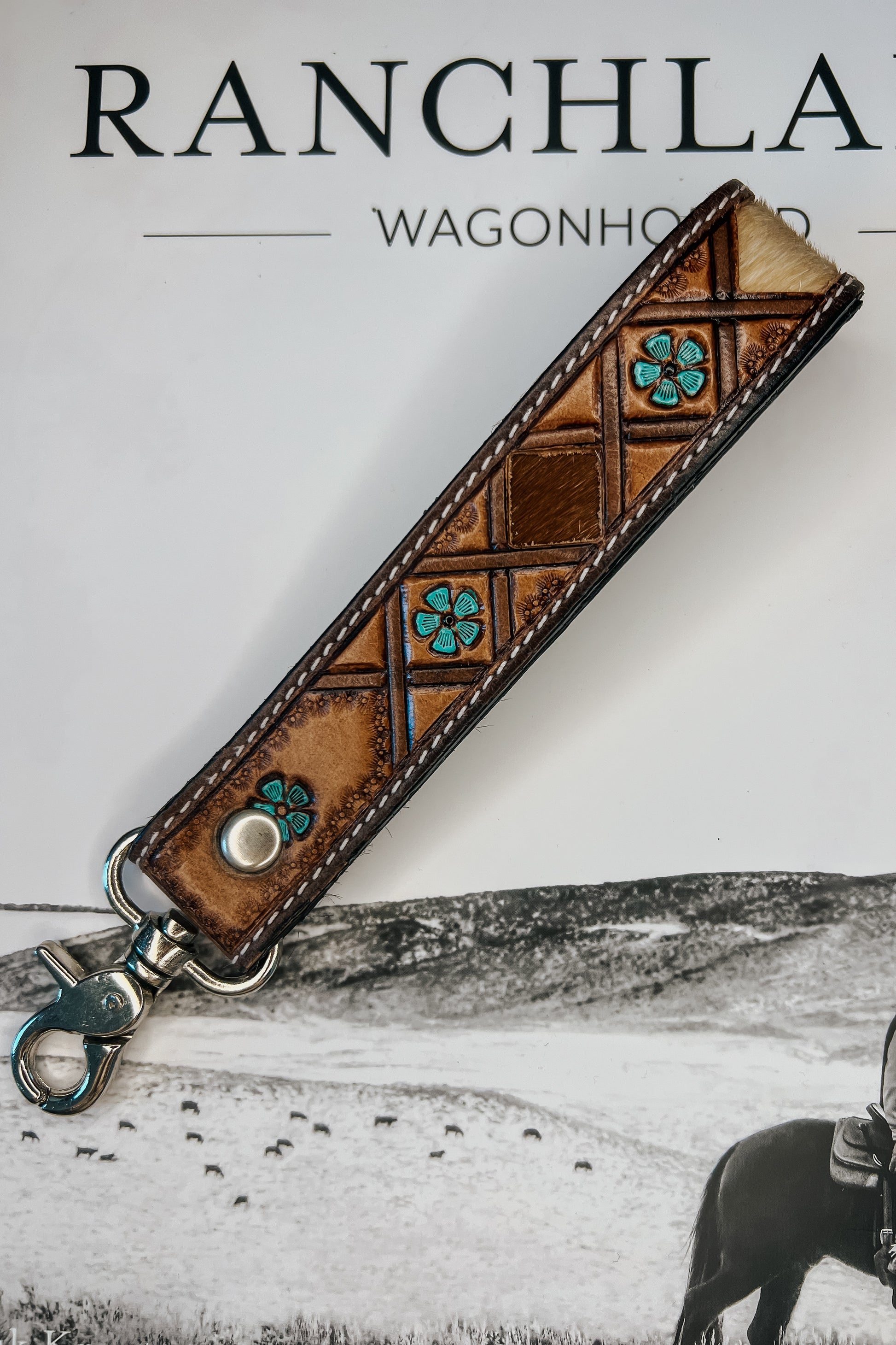 Brown leather wristlet keychain with hair-on cowhide inlay, turquoise accents, contrast stitching, and silver swivel clasp.