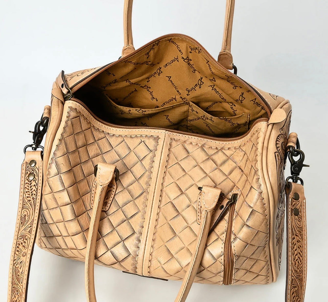 Top view of hand-tooled leather duffel bag showing zippered opening and interior pockets.