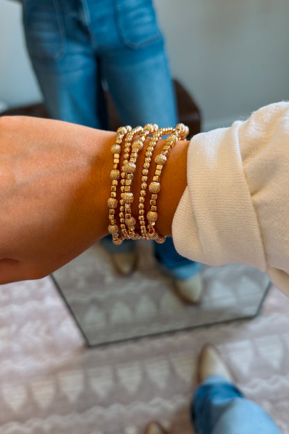A close-up of a person's wrist wearing a stack of gold beaded bracelets