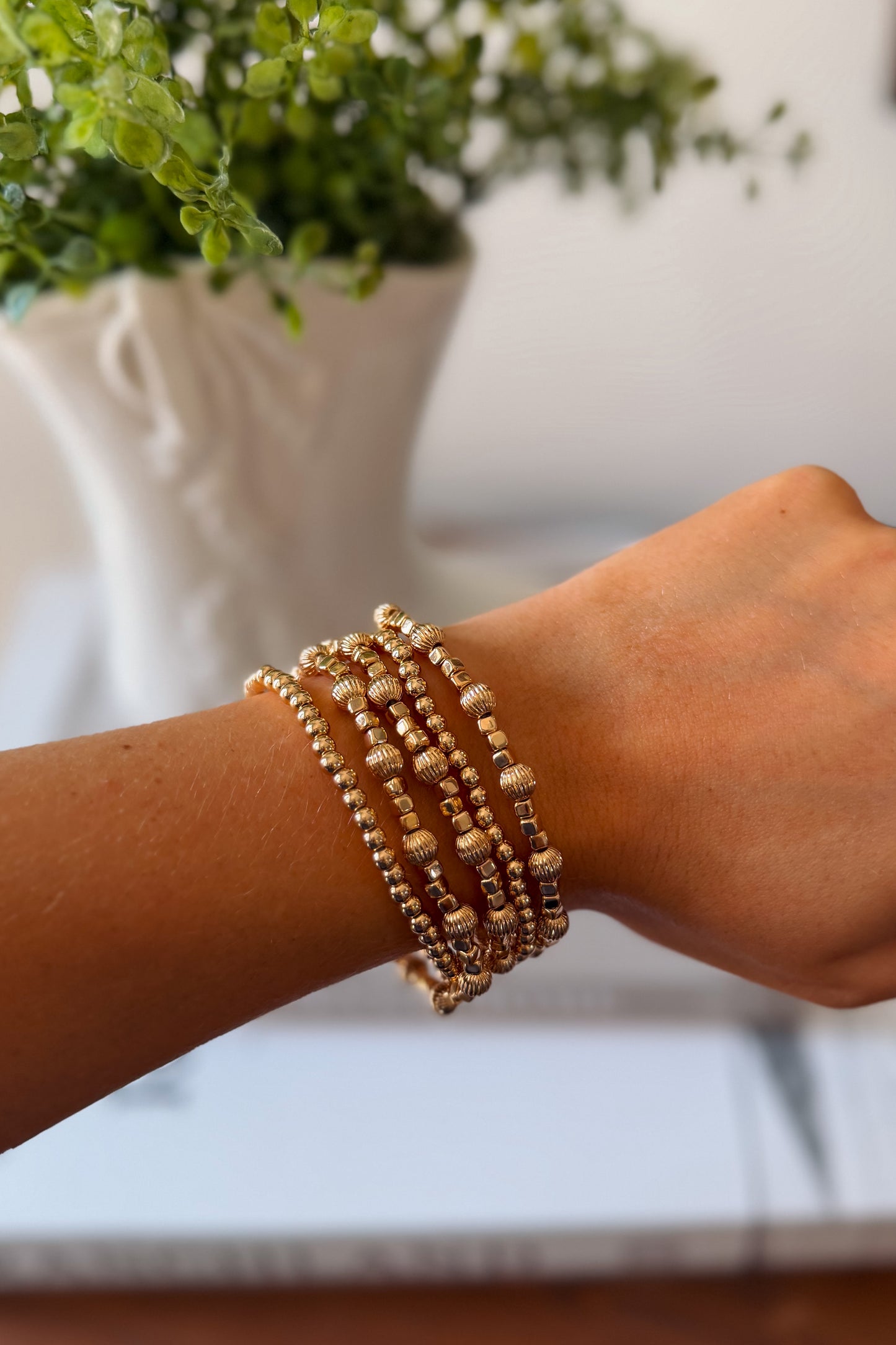 A close-up of a person's wrist wearing a stack of gold beaded stretch bracelets