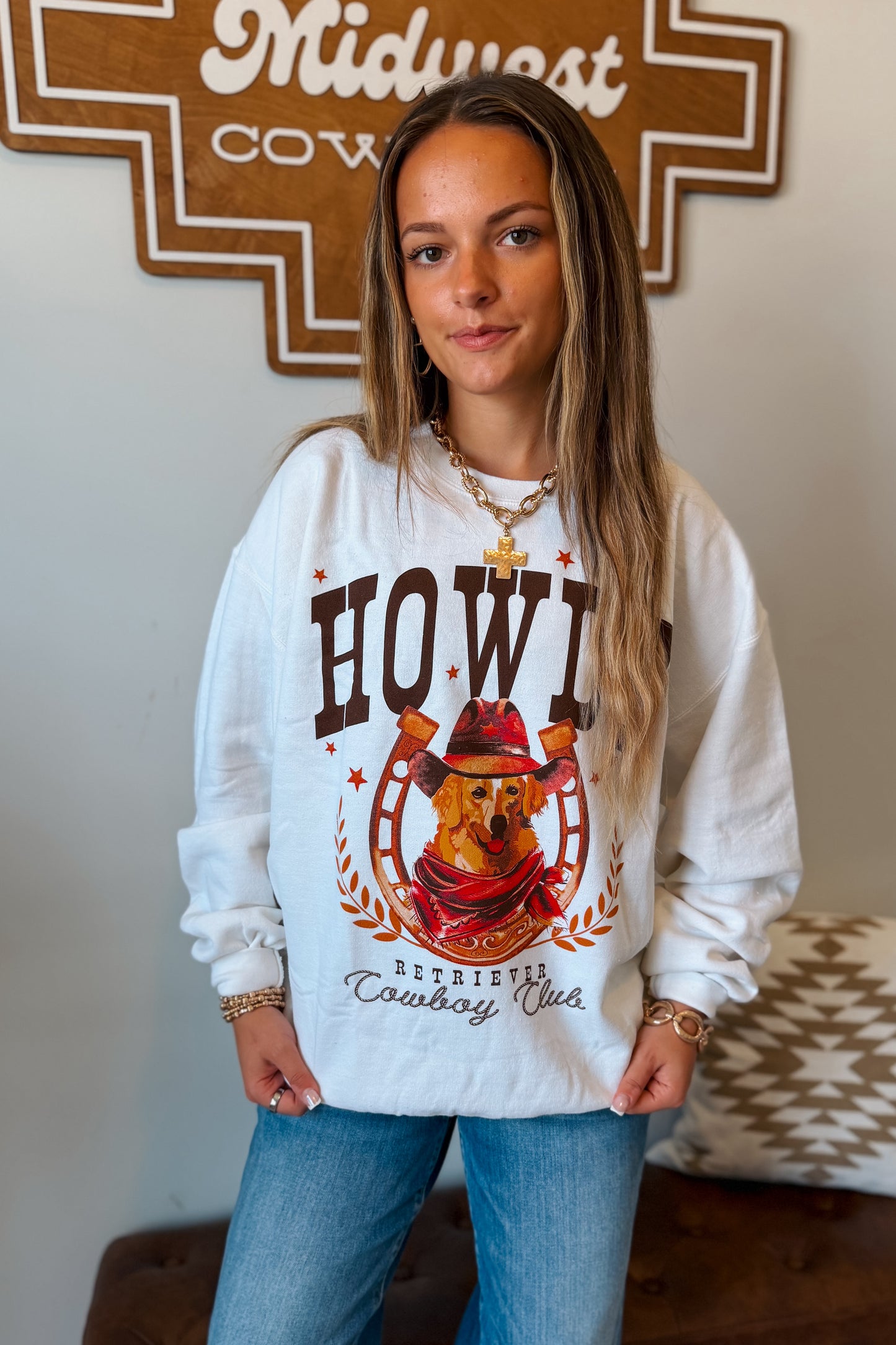 Off white crewneck sweatshirt with a rustic brown and orange graphic of a golden retriever on a horseshoe, paired with blue jeans