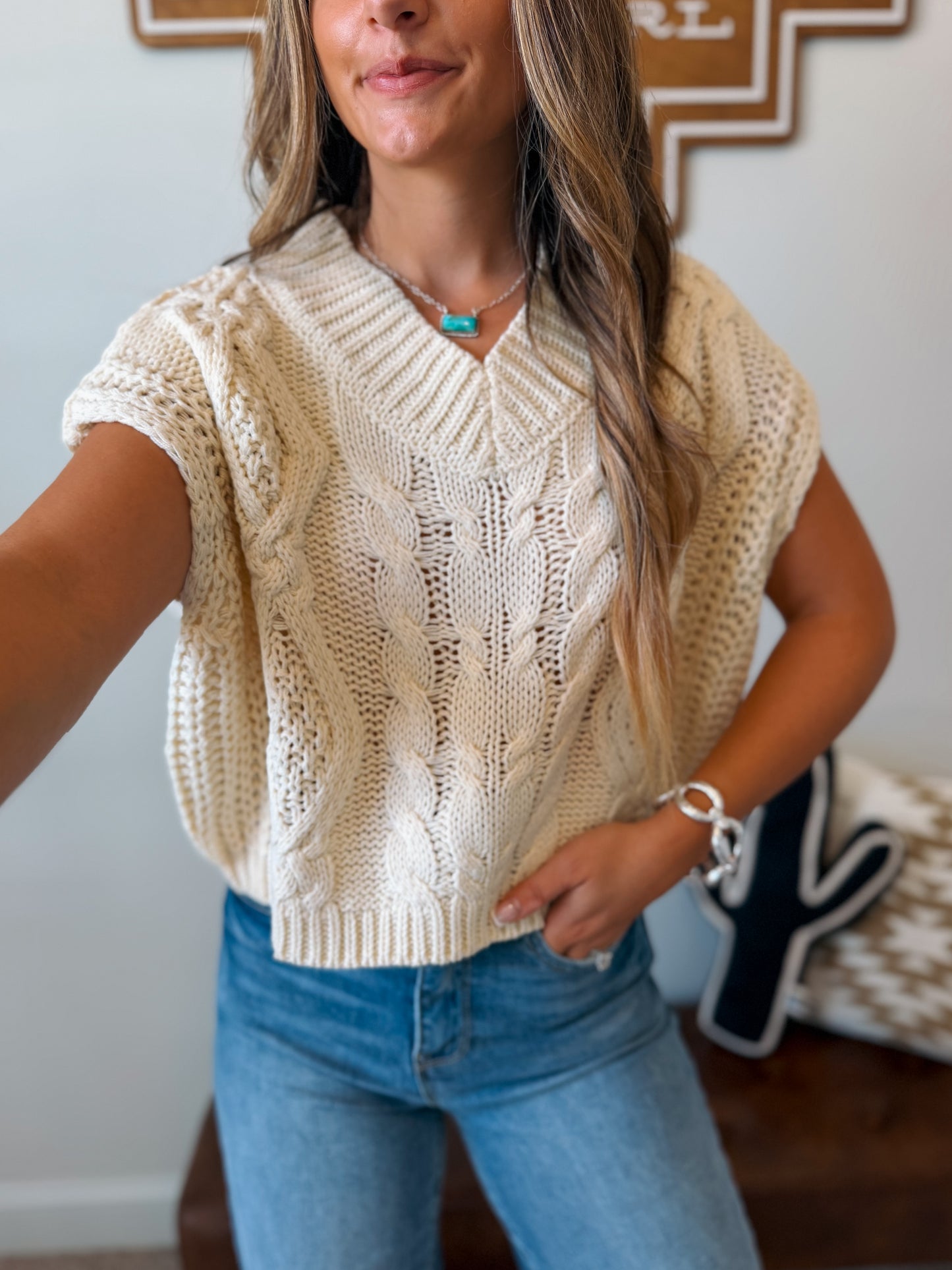 A woman wearing a cream cable-knit short-sleeve sweater vest with a V-neck, 