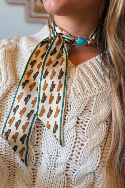 A close-up of a person wearing a patterned silk neck scarf tied with Kingman turquoise scarf slide.