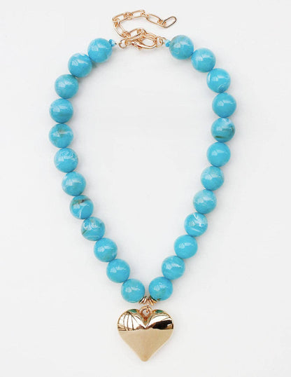 A turquoise blue beaded necklace with a polished gold heart pendant and gold clasp, displayed on a clean white background.
