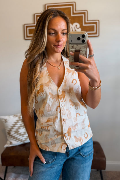 A woman wearing a sleeveless cream vest with a tan horse and paisley print, paired with blue jeans