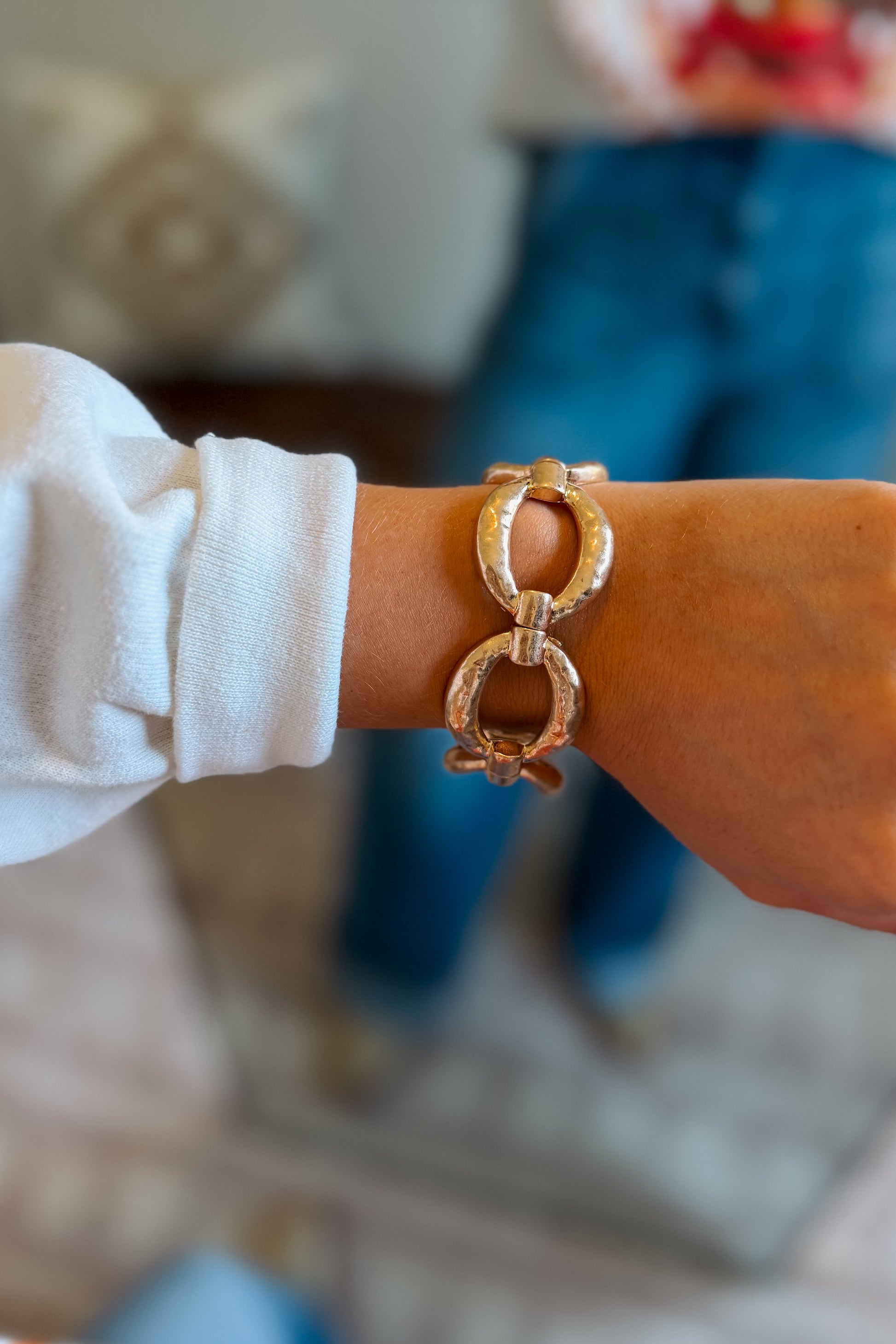 A close-up of a person's wrist wearing a chunky, textured gold-tone ring link cuff bracelet. 