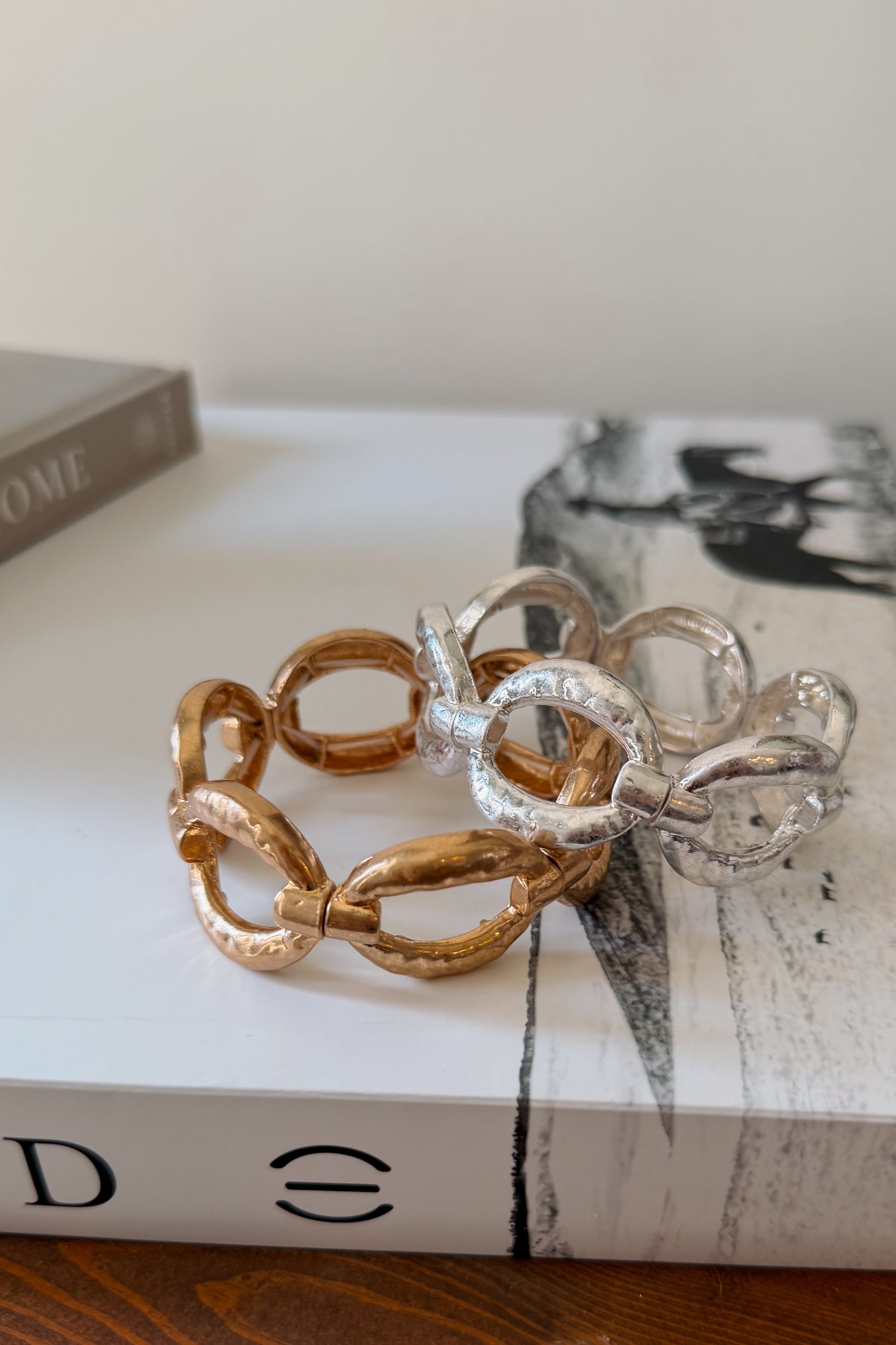 Two textured link bracelets, one gold-toned and one silver-toned, displayed on a white book.
