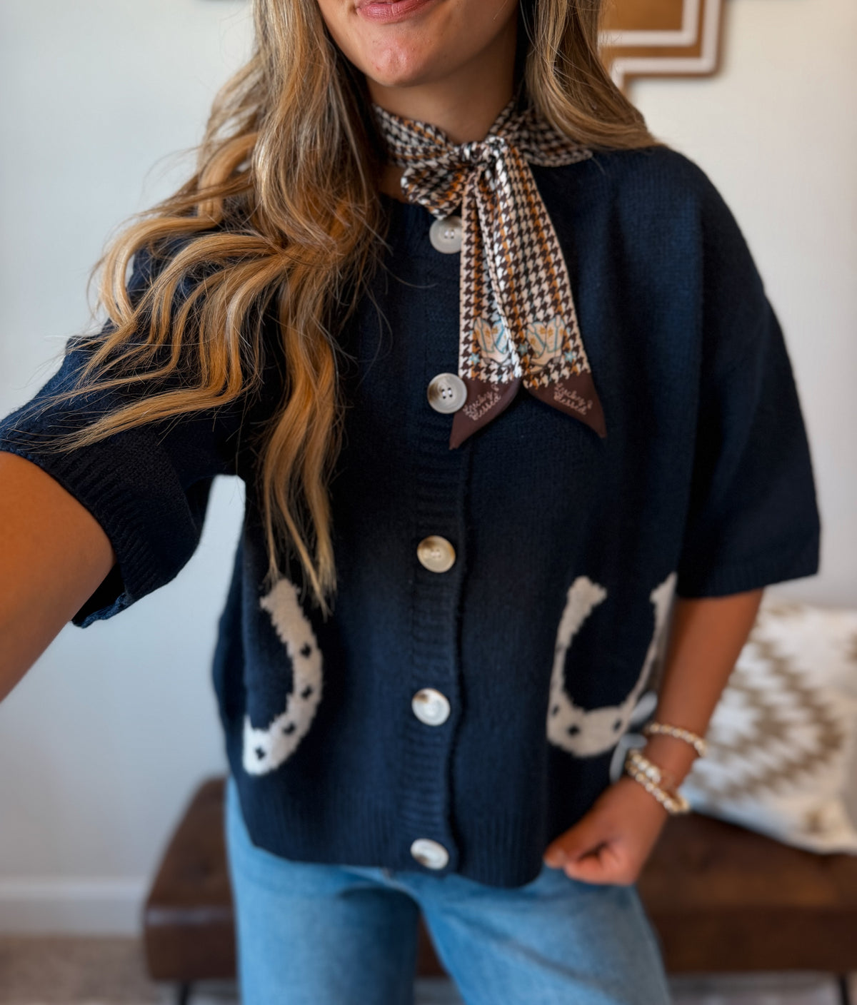 A woman wearing a navy blue knit cardigan with white horseshoe motifs on the pockets, a brown and beige houndstooth necktie