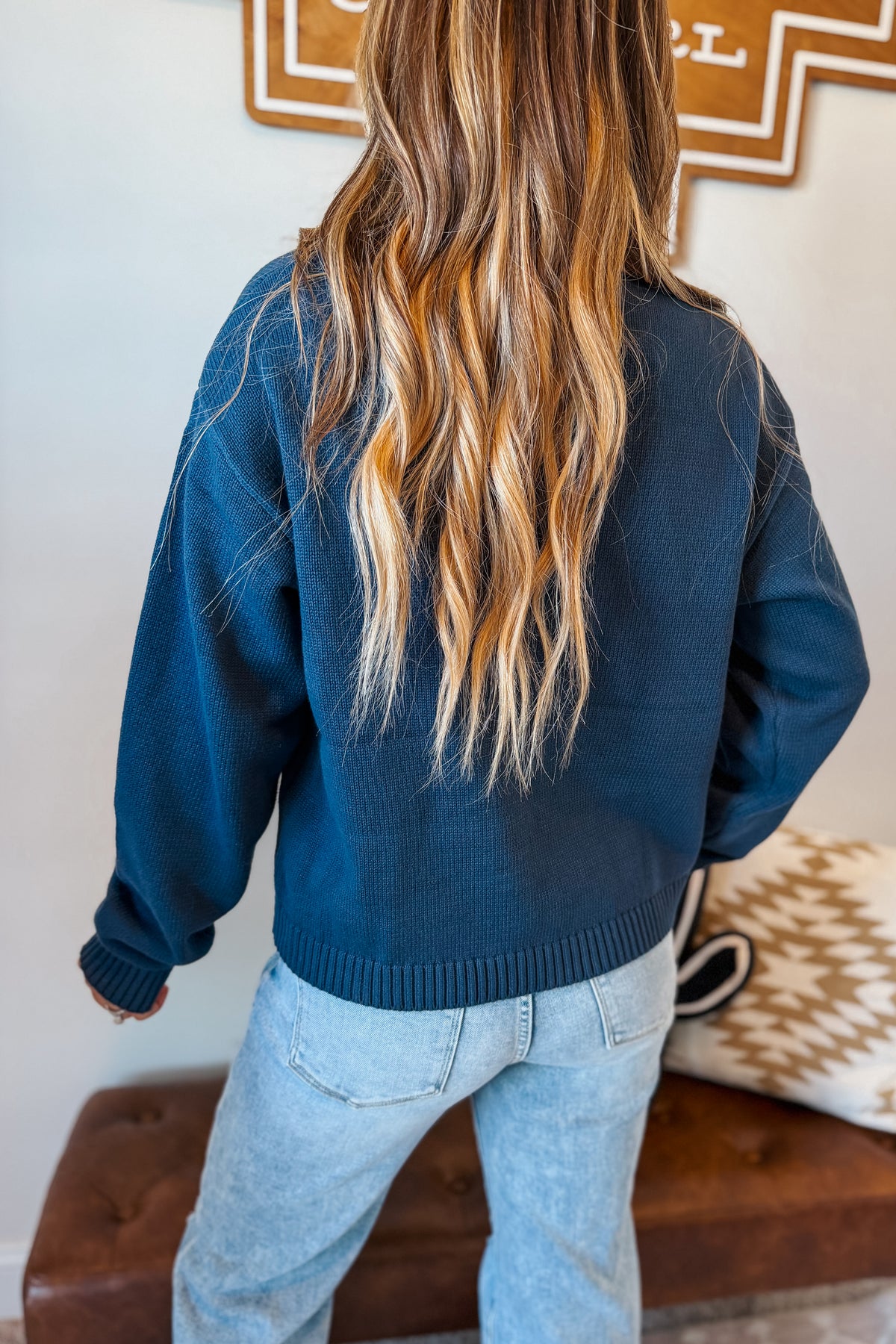A woman viewed from behind wearing a dark navy blue knit sweater and light wash jeans