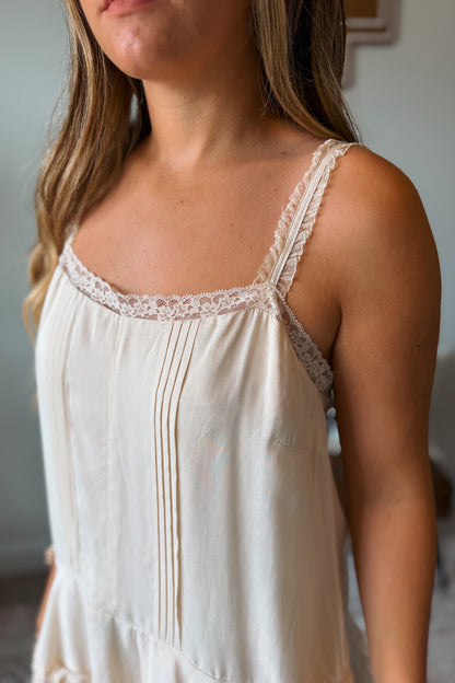 A close-up of a woman wearing a cream-colored cotton slip dress with delicate lace trim along the scoop neckline and thin spaghetti straps.