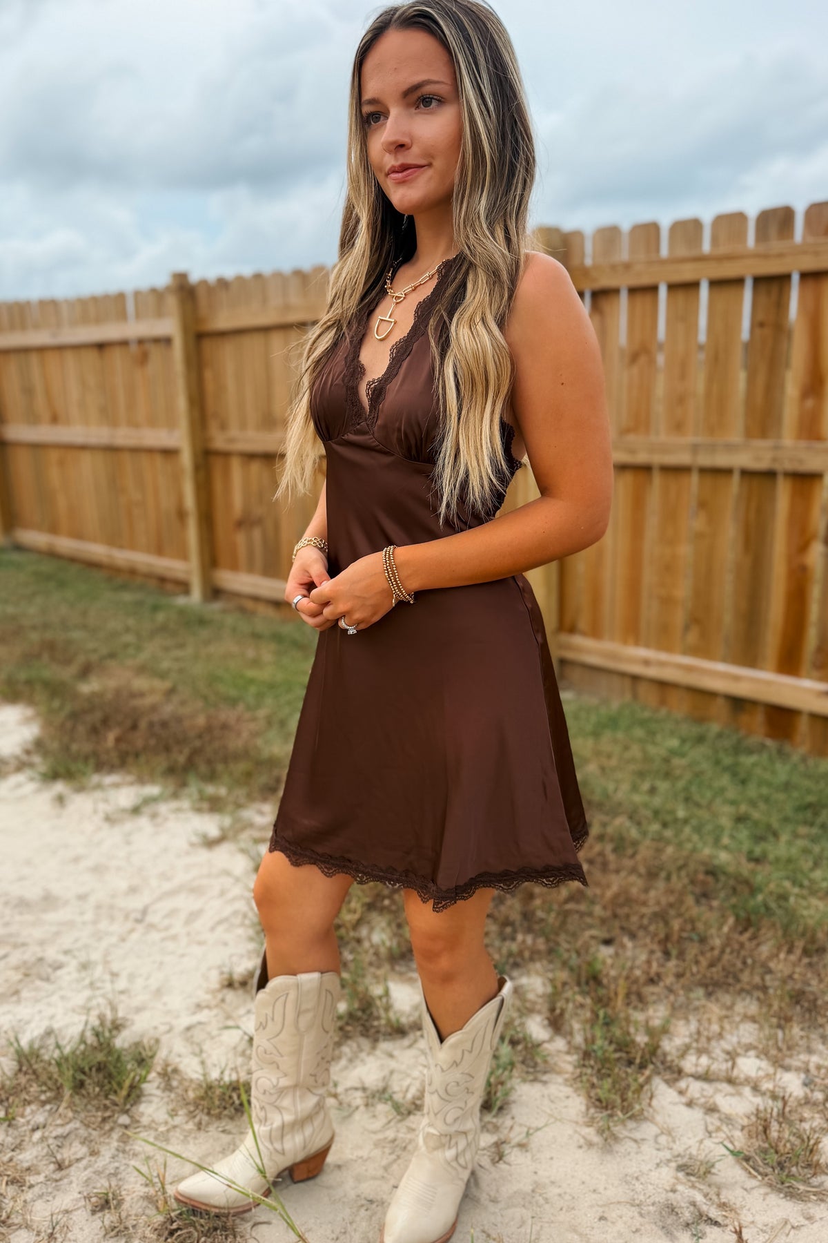 Side view of A woman wearing a brown satin slip dress with lace trim and white cowboy boots,