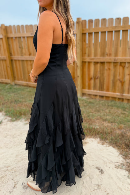 A woman wearing a black spaghetti-strap maxi dress with a ruffled tiered skirt.