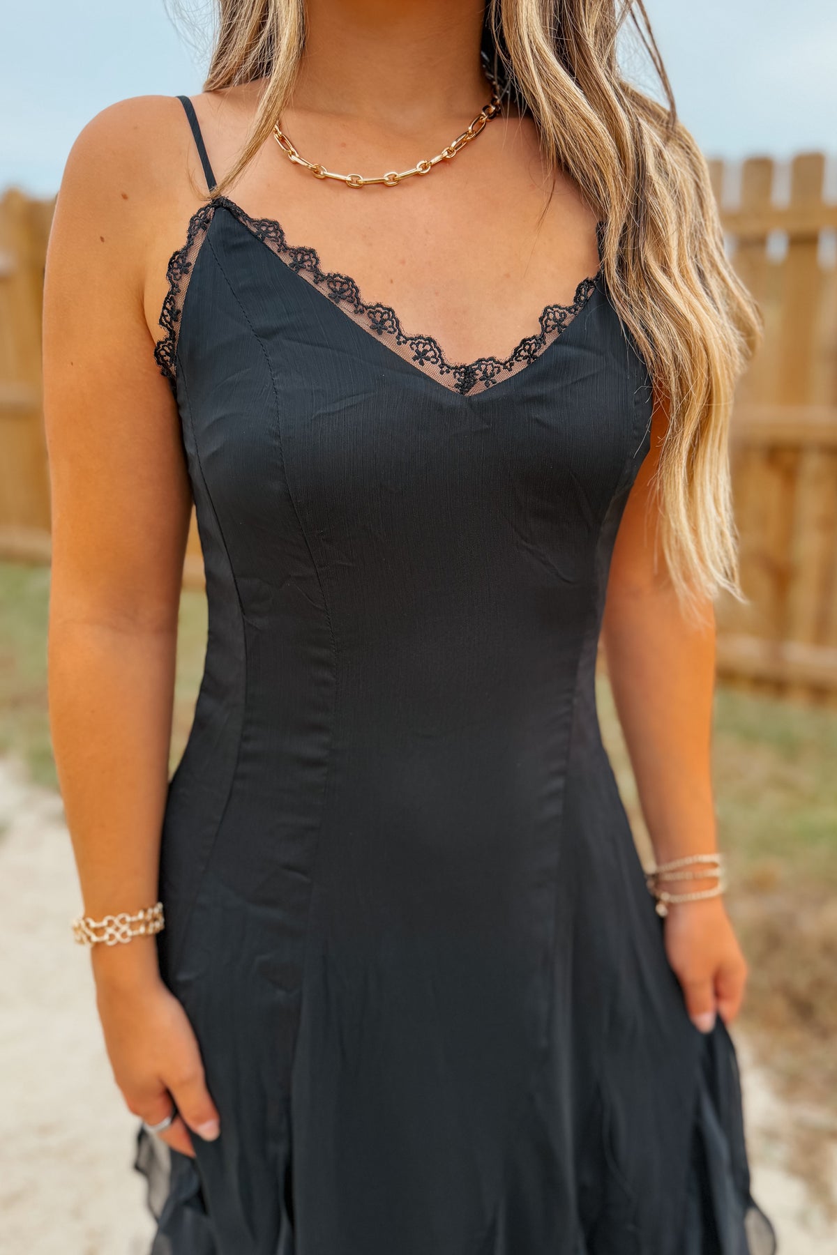 A woman wearing a black spaghetti-strap dress with black lace trim along the neckline.