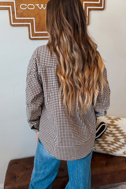 A woman viewed from behind wearing a brown and white and brown gingham long-sleeve button-up shirt and blue jeans
