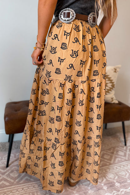 Back view of a tan maxi skirt with a black cattle brand pattern throughout. Features a stretchy elastic waistband and a relaxed, flowing fit.