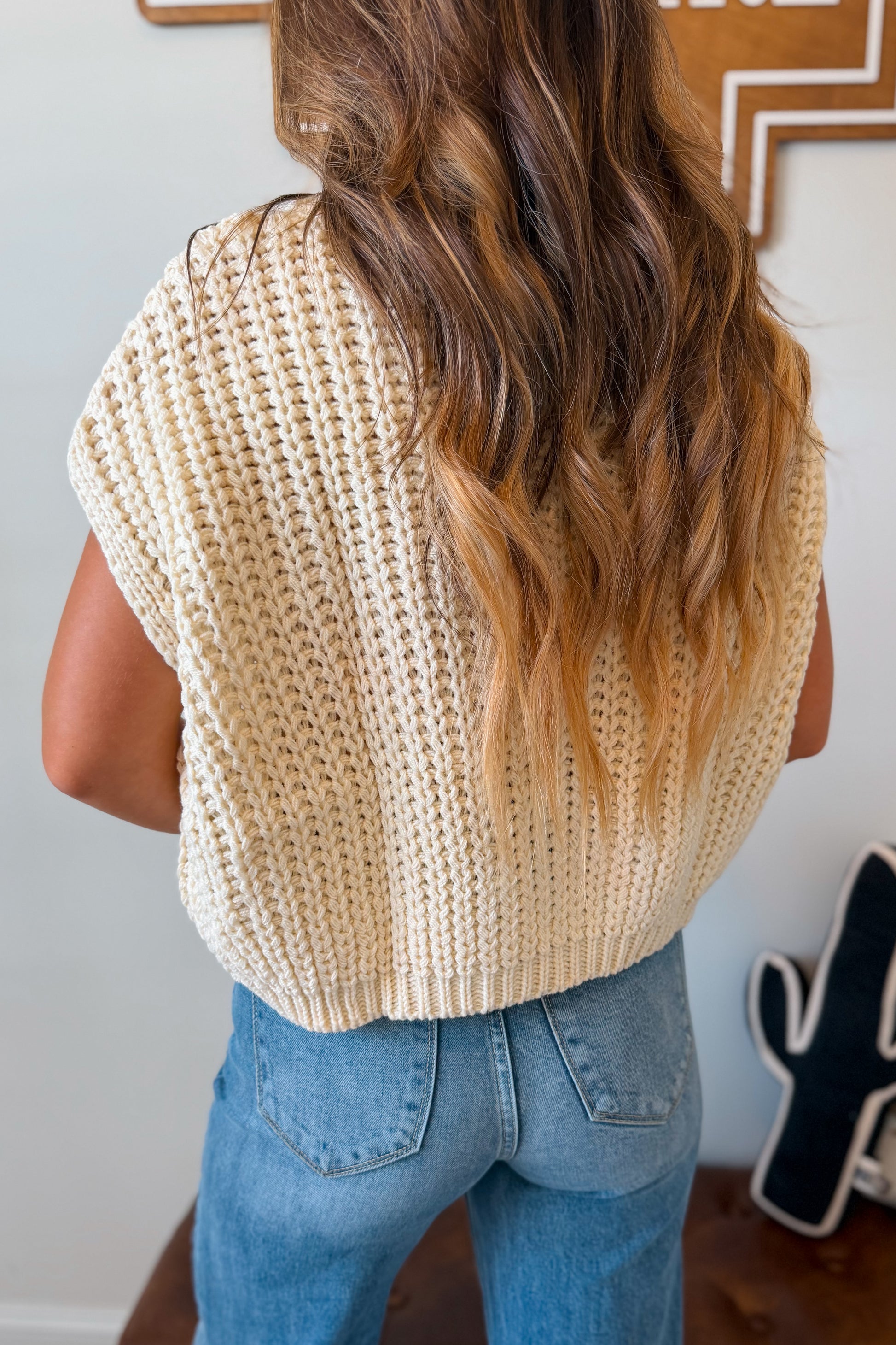 A woman viewed from behind wearing a cream-colored, chunky knit short-sleeve top 