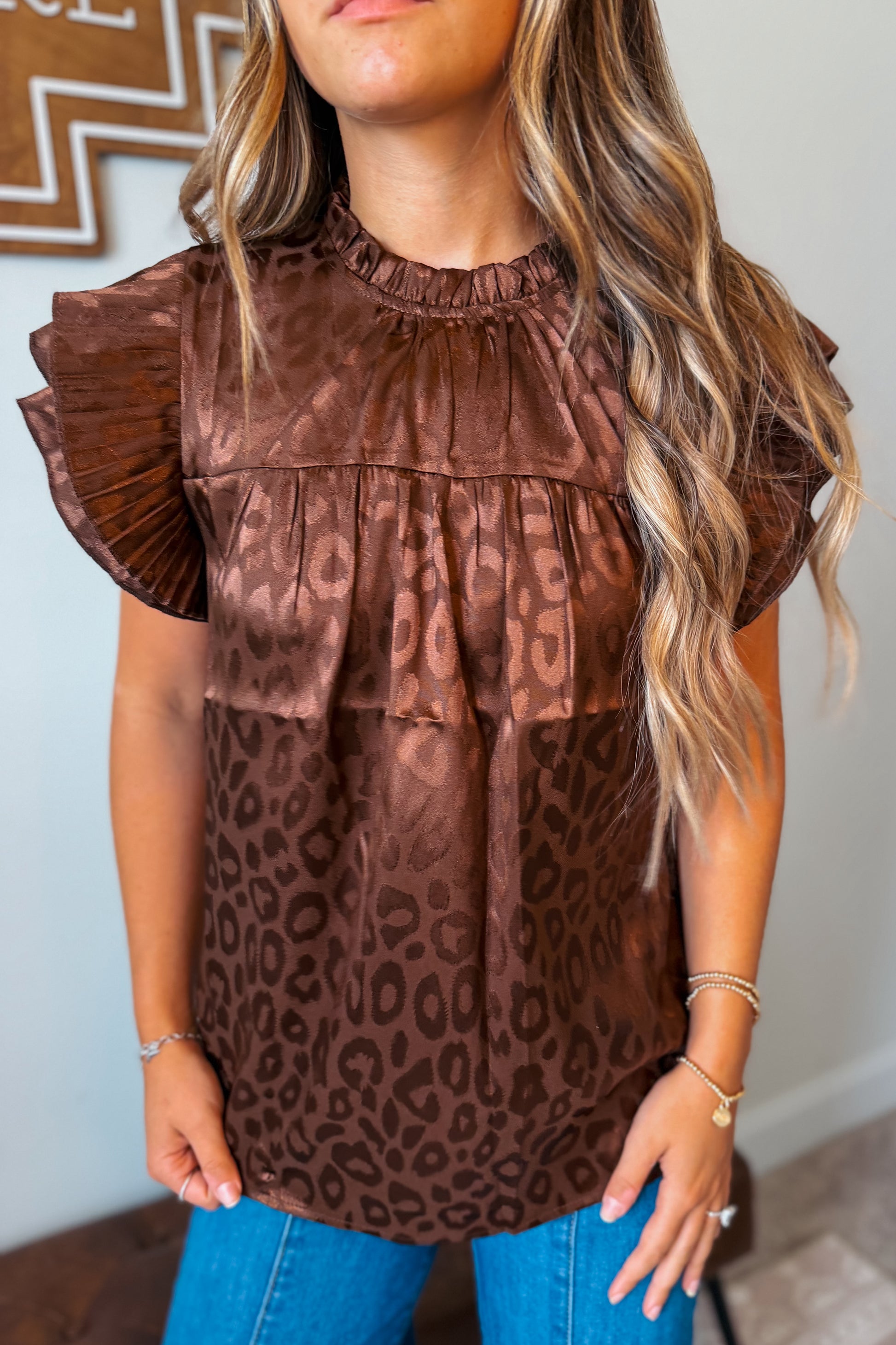 Close-up view of a brown leopard print top highlighting the ruffle sleeve detail, lightweight fabric, and allover animal print pattern.
