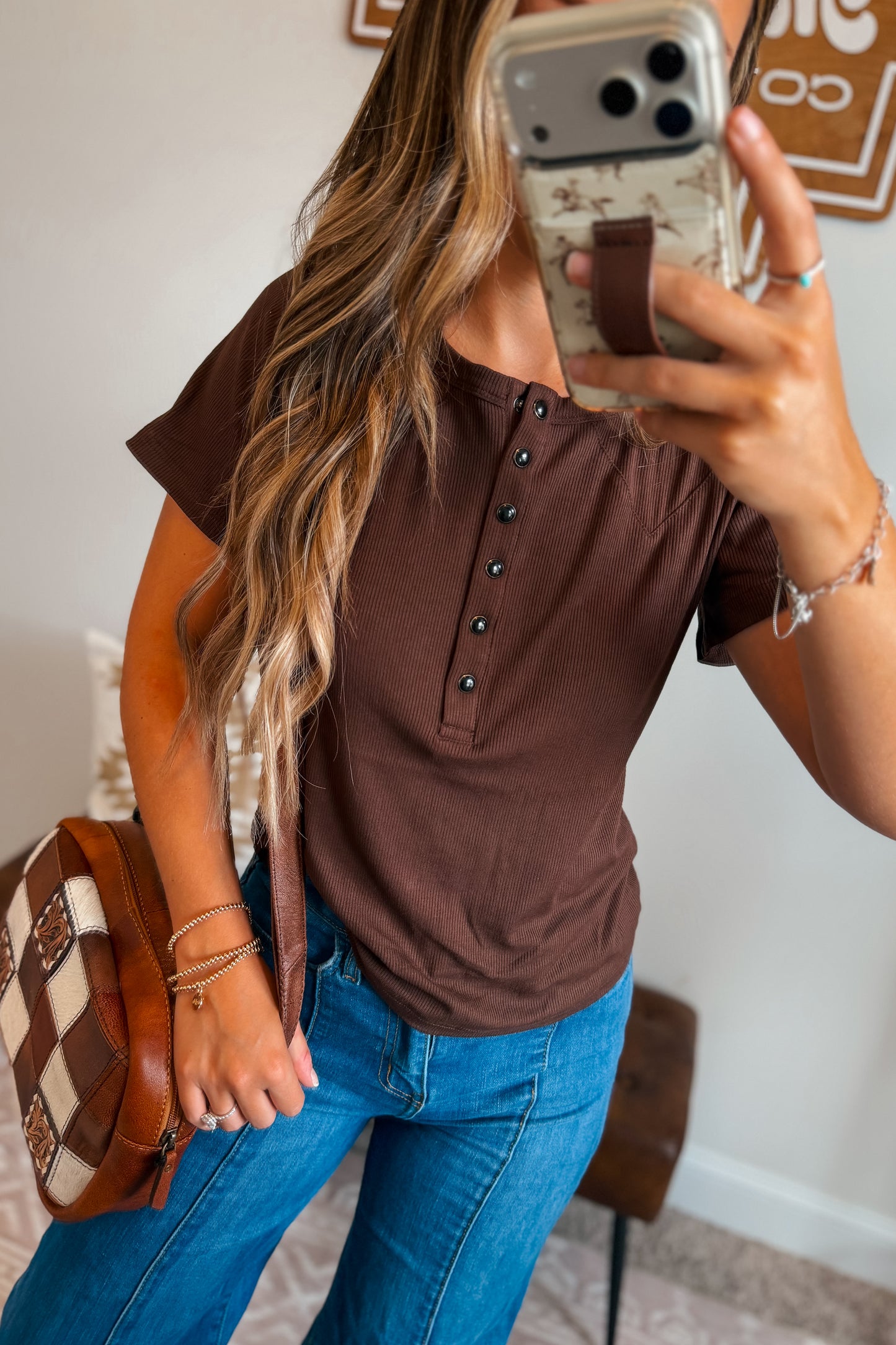 Brown ribbed knit top featuring a quarter-button neckline, short sleeves, and a fitted silhouette. Designed with a soft textured fabric for comfortable everyday wear.