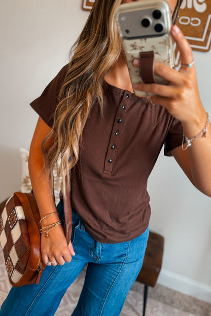 Brown ribbed knit top featuring a quarter-button neckline, short sleeves, and a fitted silhouette. Designed with a soft textured fabric for comfortable everyday wear.