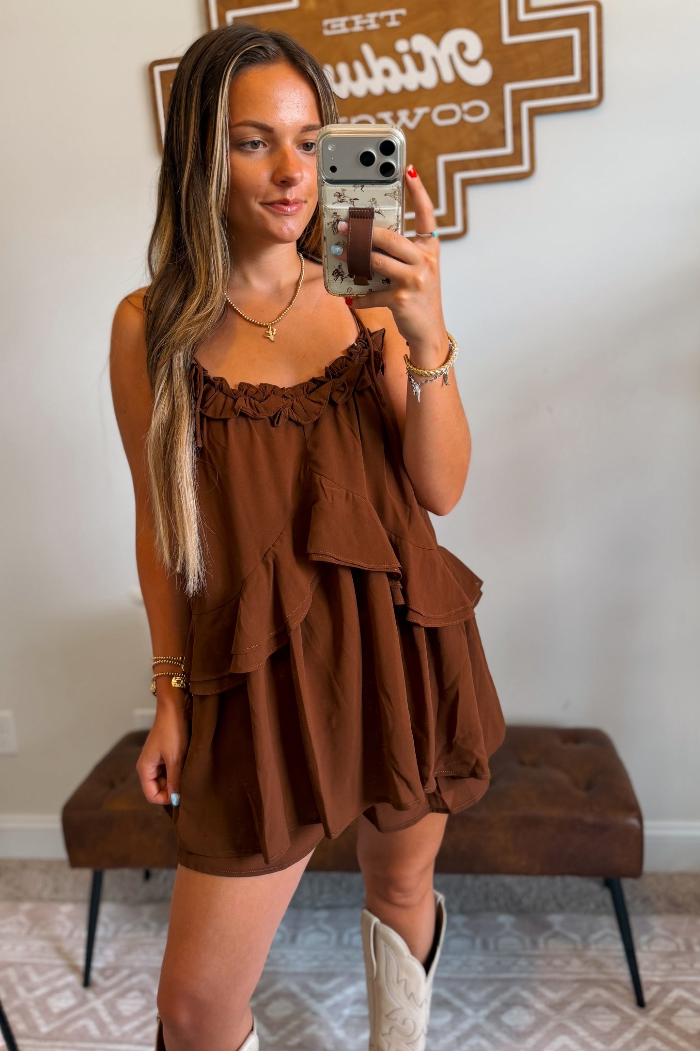 Front view of brown flowy romper featuring adjustable tie straps and layered ruffle details.