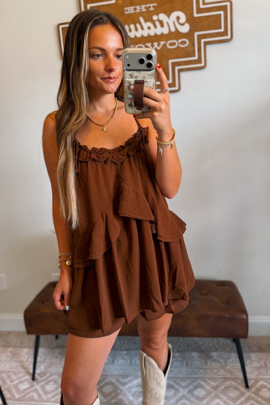 Front view of brown flowy romper featuring adjustable tie straps and layered ruffle details.