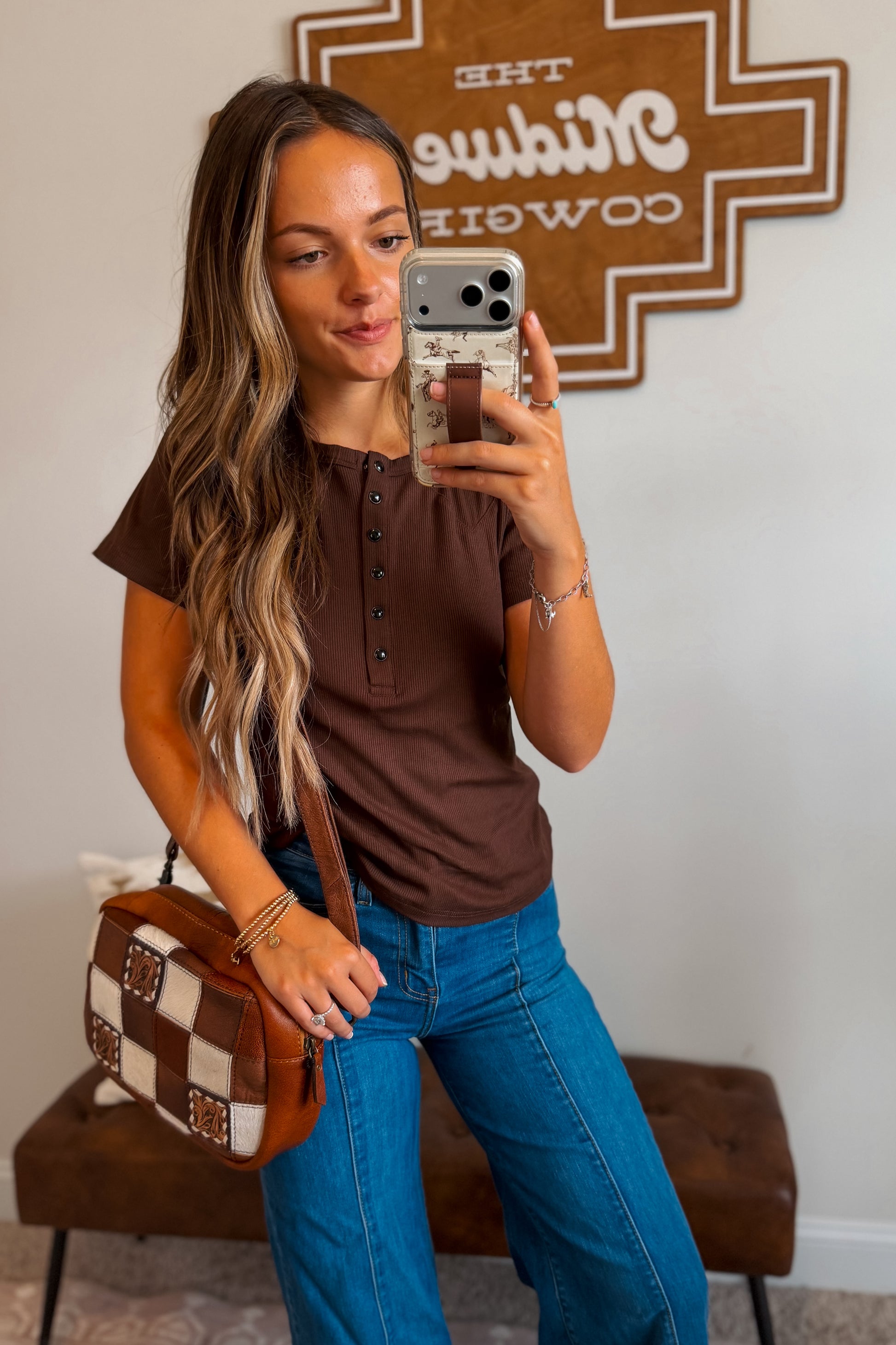 Model wearing a brown ribbed knit top featuring a quarter-button neckline and fitted silhouette, styled with denim bottoms for a casual western-inspired look.
