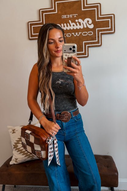 Model wearing a gray mineral wash cropped tank top featuring a vintage cowboy collage graphic and tan piping accents, styled with denim bottoms.