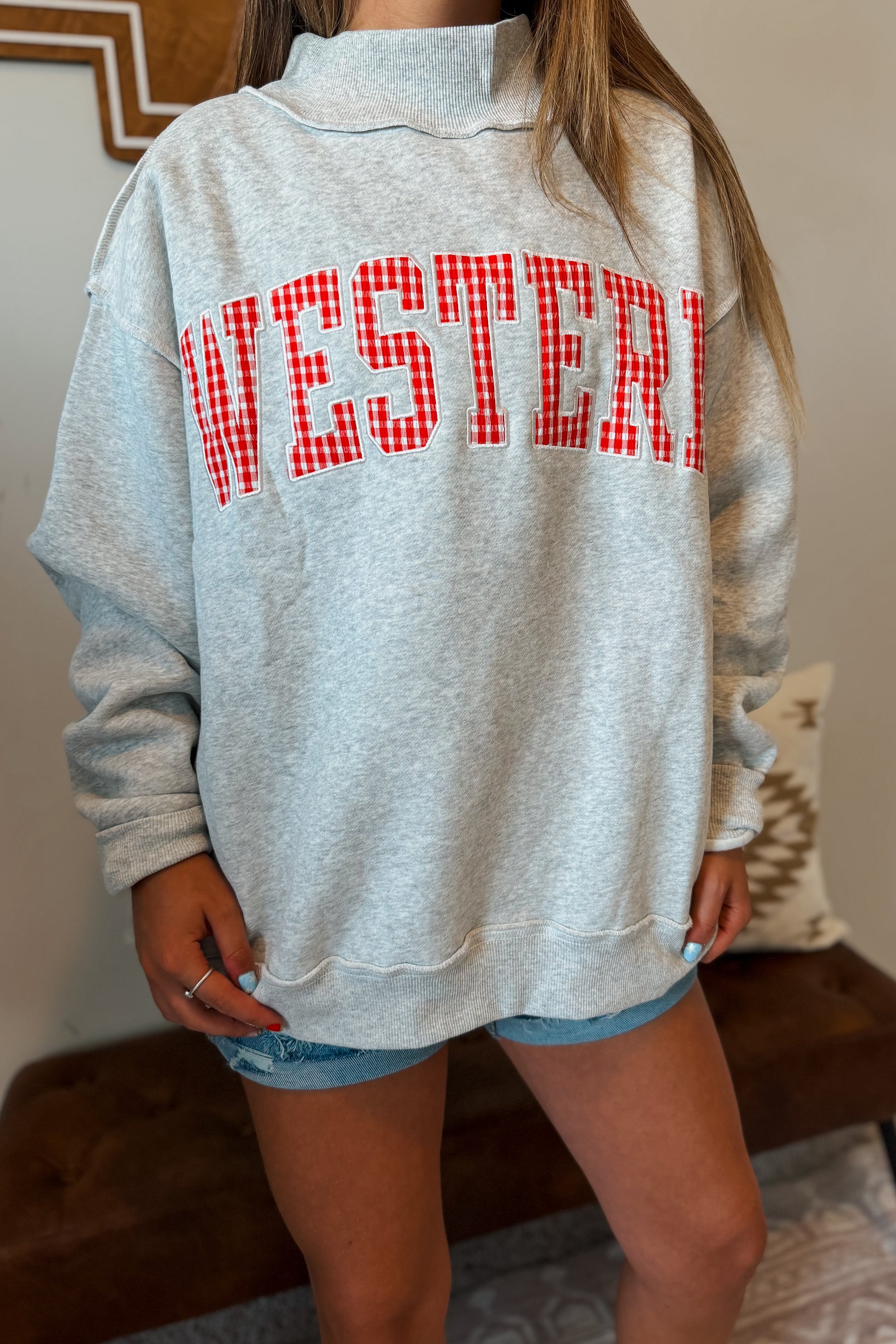 Close-up of “WESTERN” embroidery with red gingham plaid fabric inlay on a gray mock neck sweatshirt.
