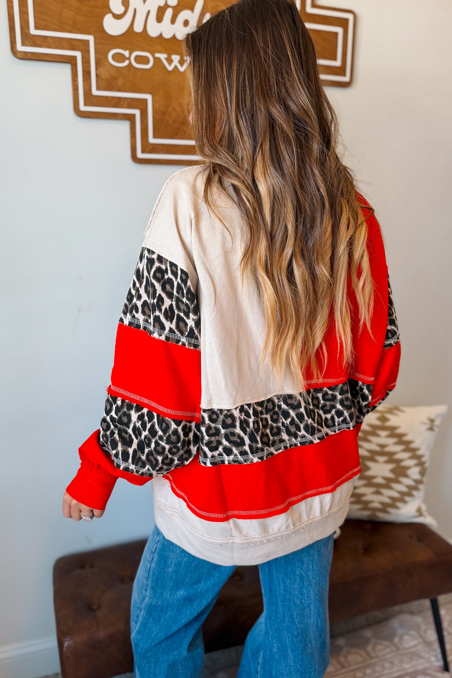A woman viewed from behind wearing a color-blocked sweatshirt with red and cream horizontal stripes and leopard print sleeves.