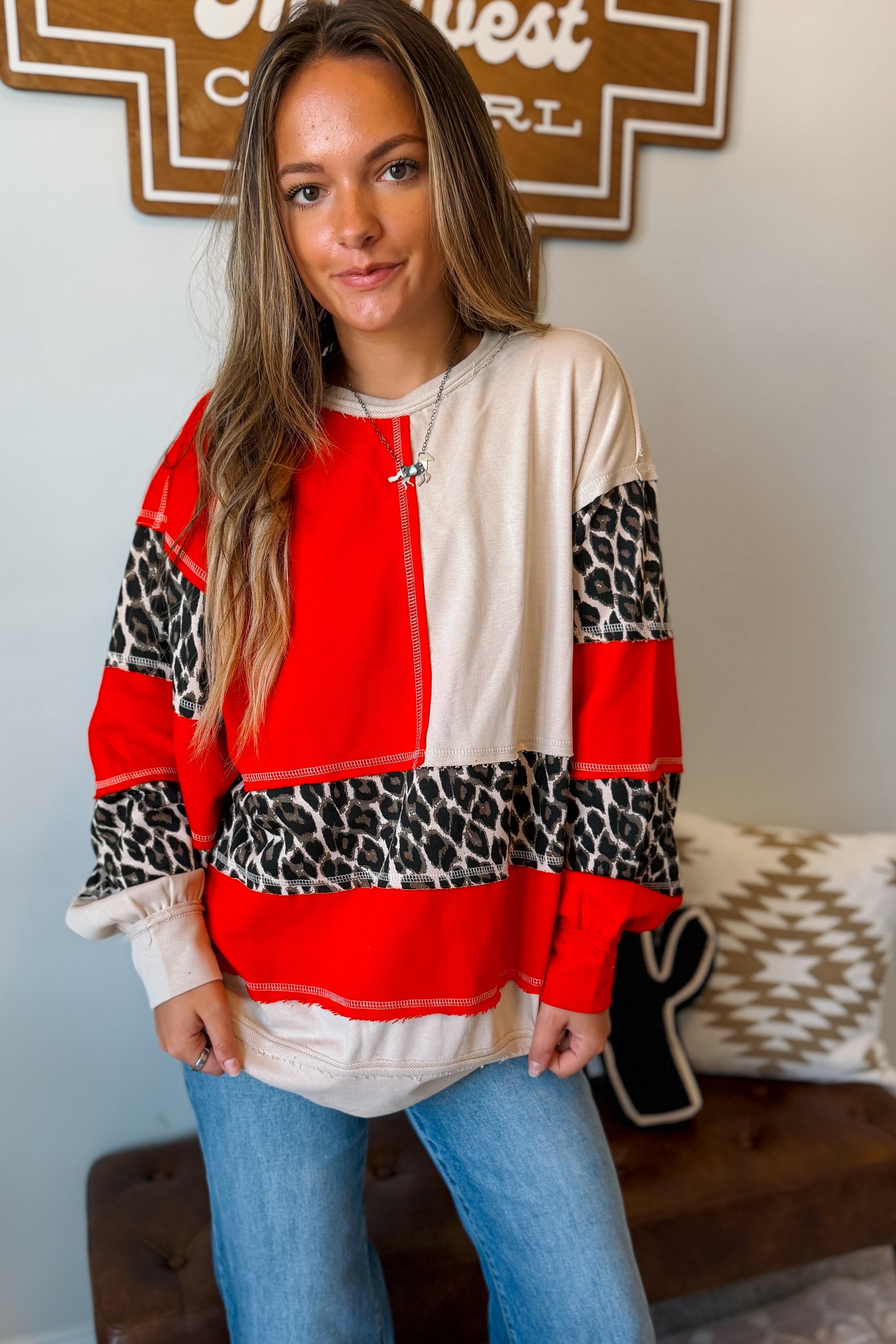 front view of A woman wearing a color-blocked long-sleeve top with red, cream, and leopard print panels.
