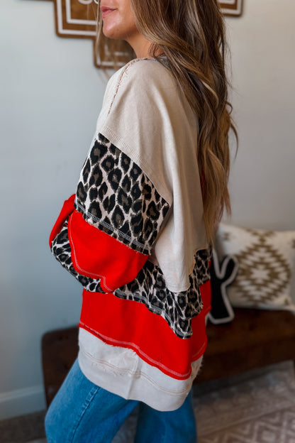 side view of A woman wearing a color-block sweatshirt with beige, red, and leopard print panels, paired with blue jeans .